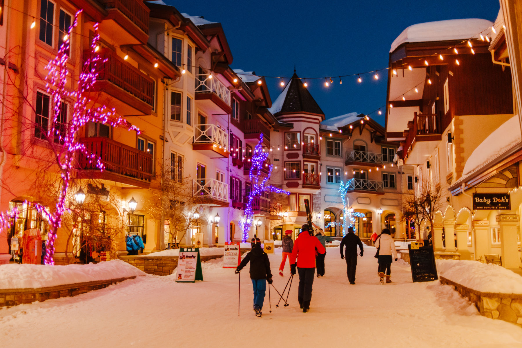 skiers walking through the village with lights hanging over them