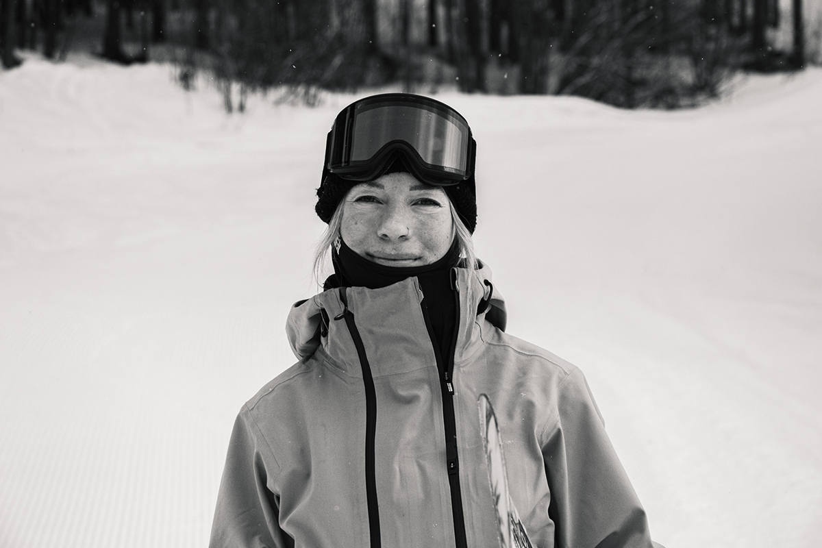 Zuzy Rocka smiles for the camera on snow. In black and white.