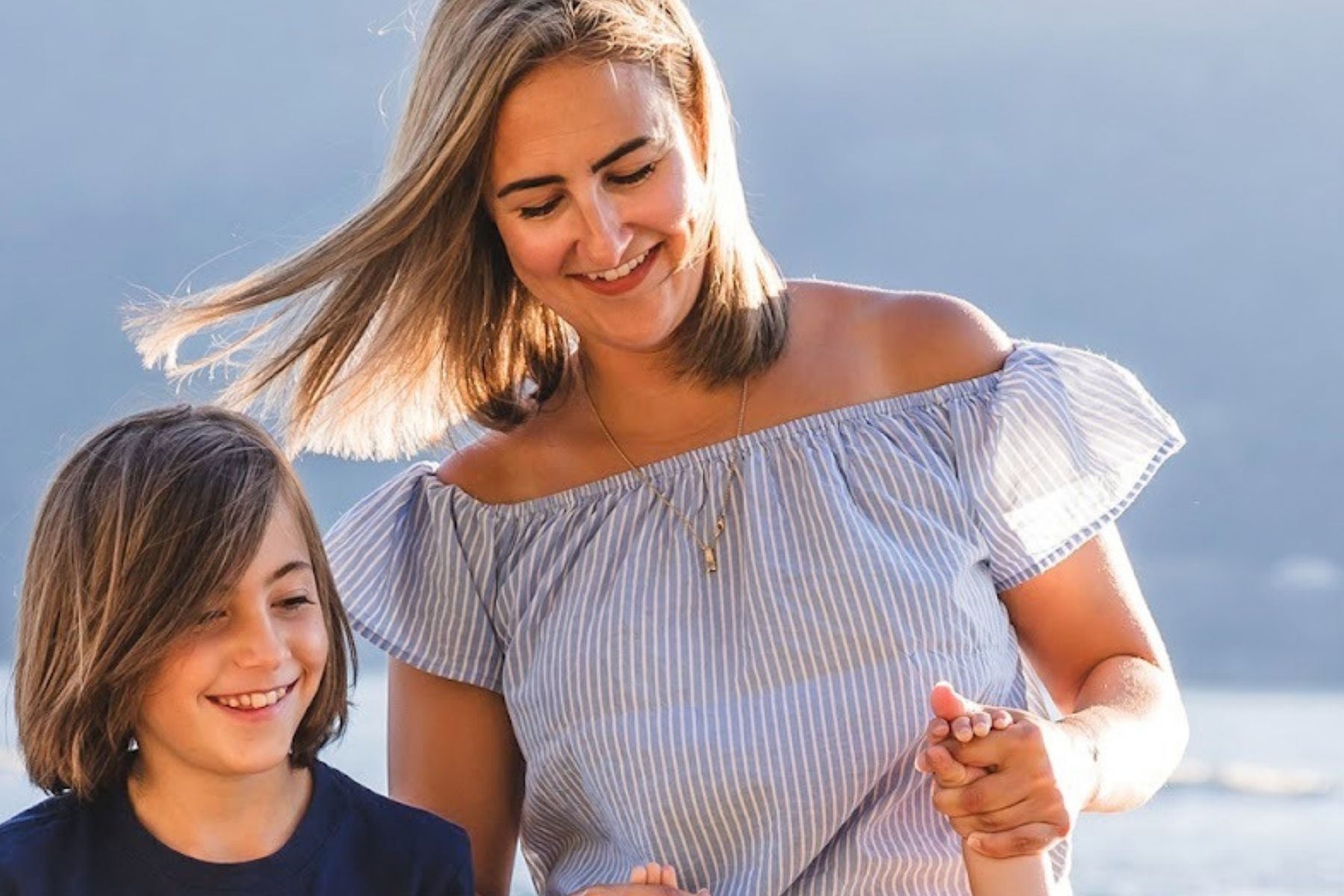 Amy Hamilton Smiles in a blue top, her son smiling beside her and she is holding another child's hands.