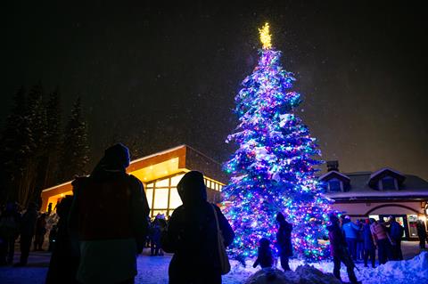 Night time view of a large lit up Christmas tree in a public square filled with people