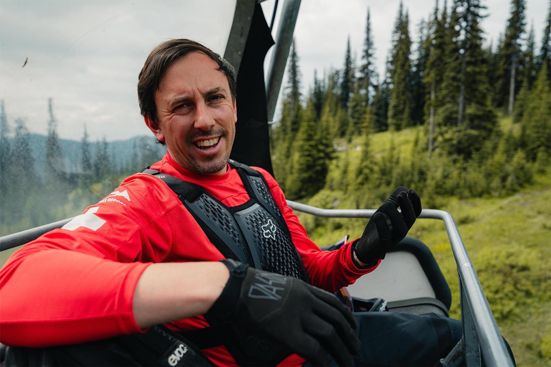 Man sitting on the chairlift talking to the camera with trees behind him.