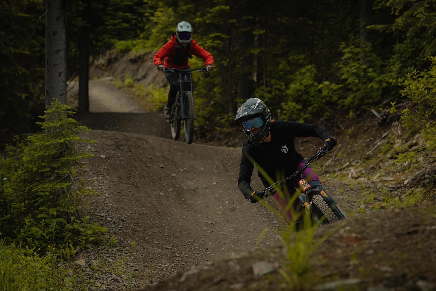 two ladies biking down a dh trail with trees around them