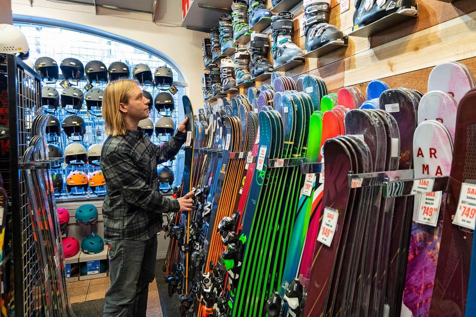 A man standing infront of snowbaords and skiis in a rental shop