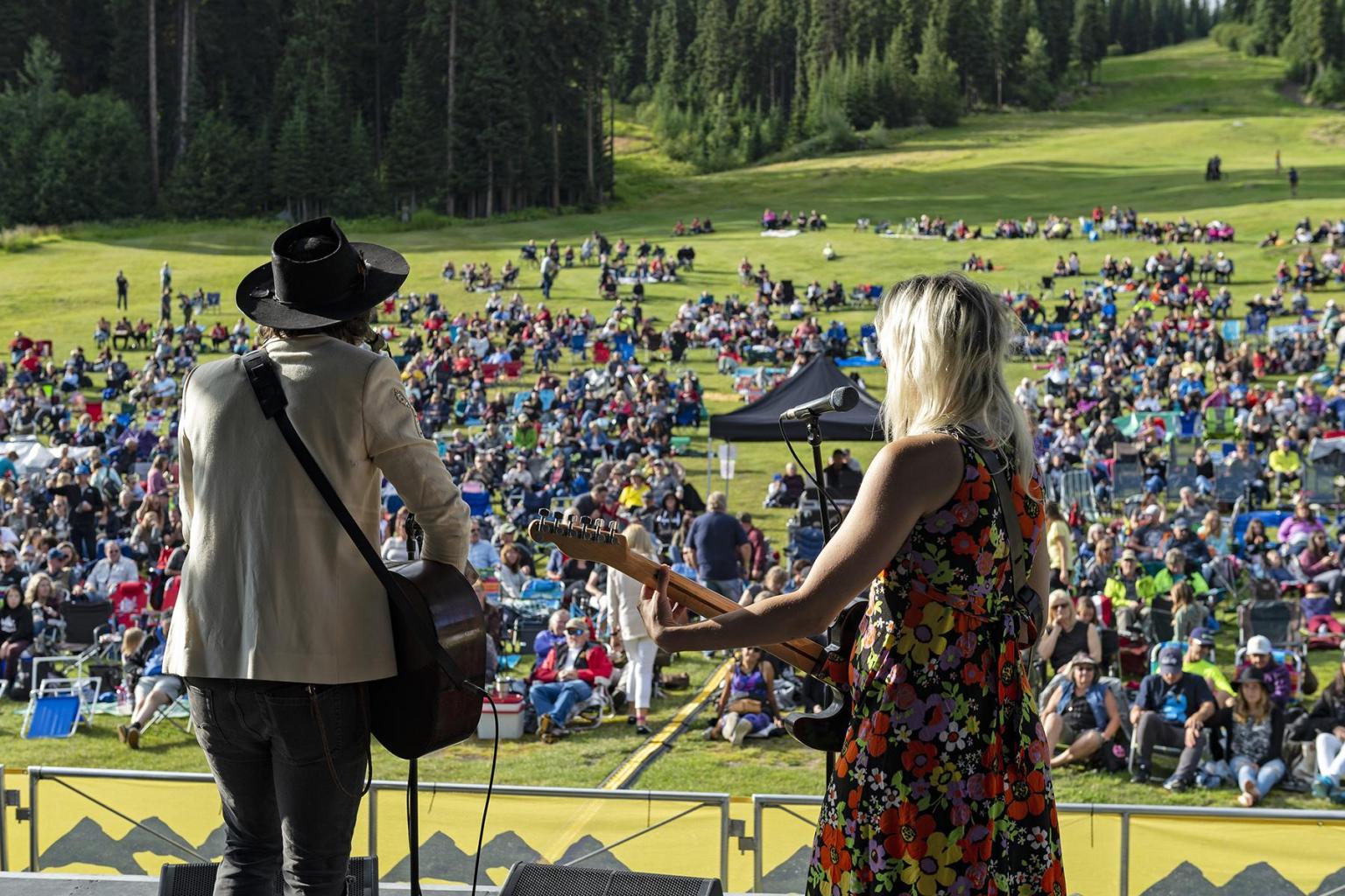 People on a stage playing music for a group of people on the mountain
