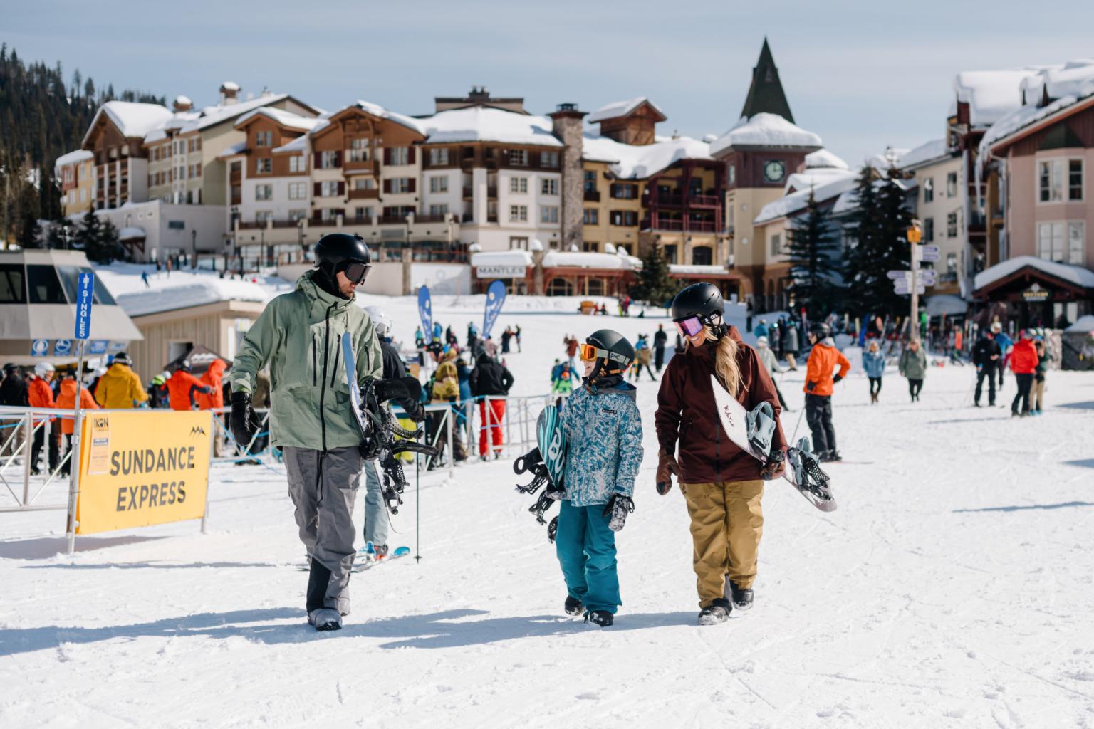 Three people walking through the snow holding their snowboards with the village in the background