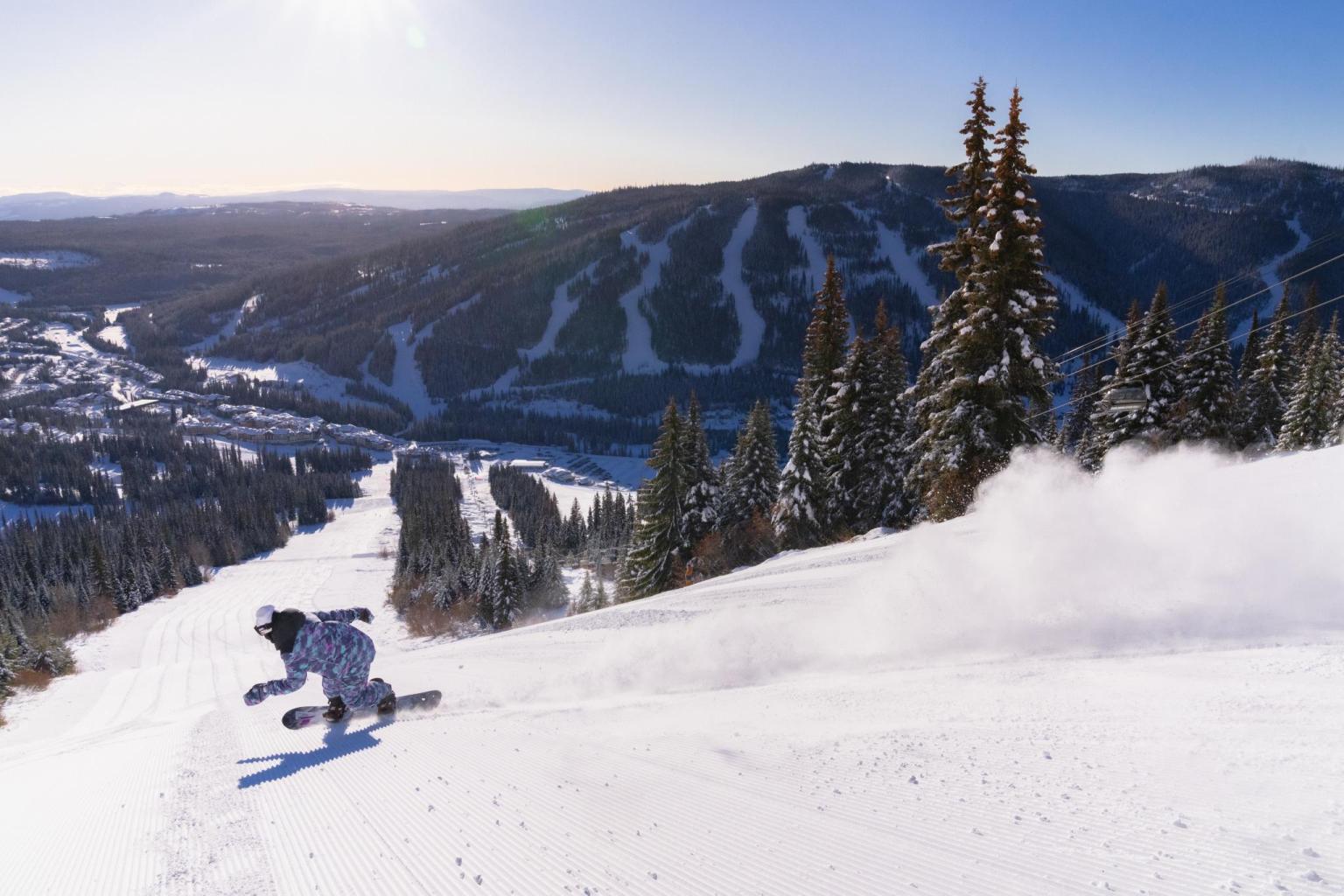 Snowboarder riding down a groomed run in spring at Sun Peaks