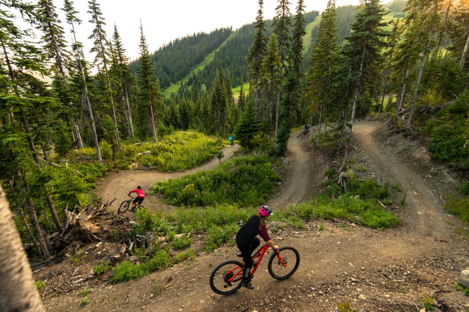 a group of bikers riding down a trail with mountain views in the background