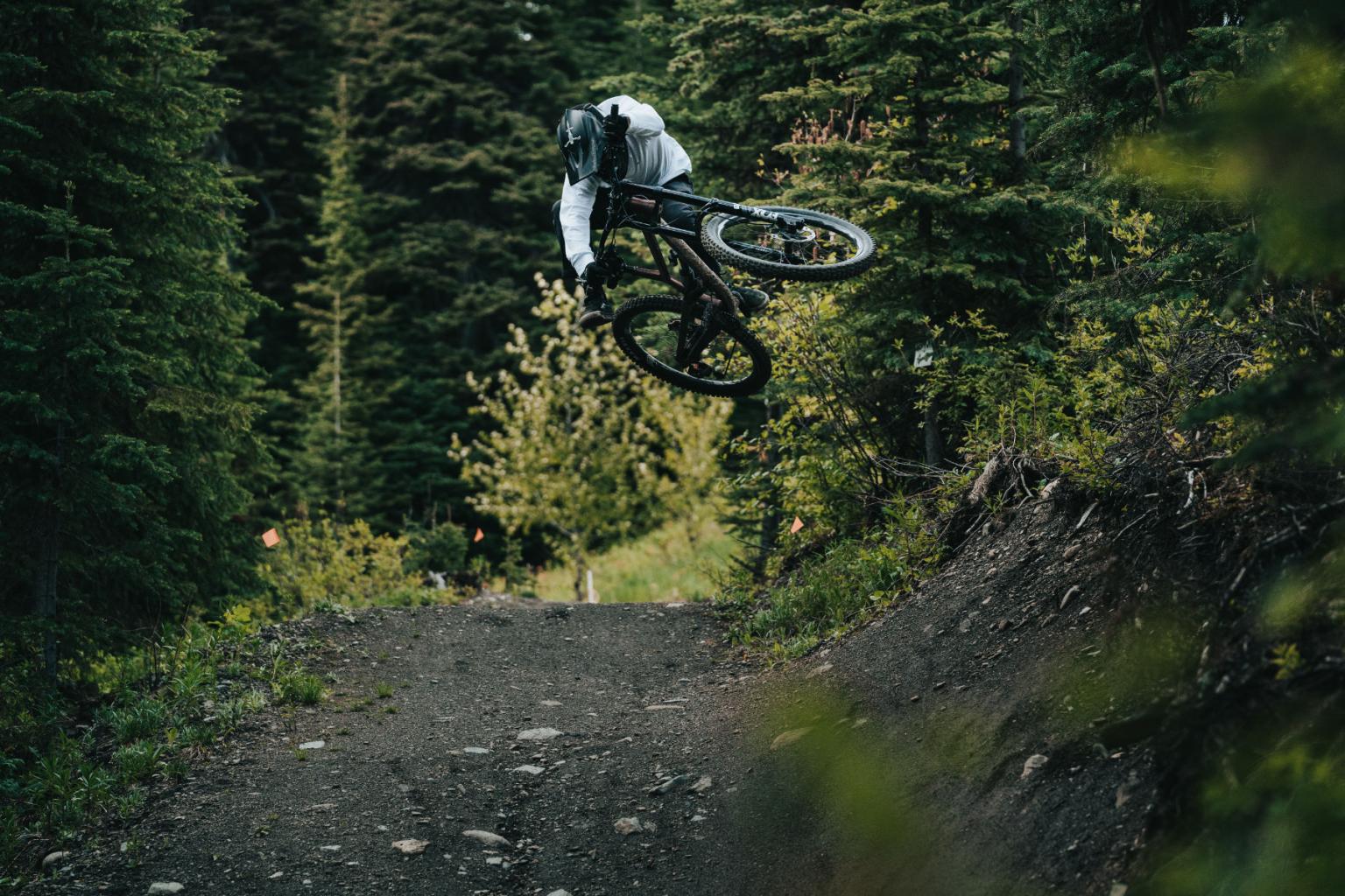 Biker hitting a jump with trees surrounding them