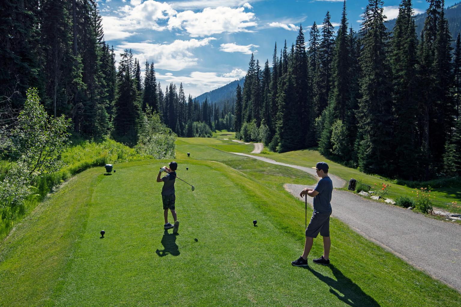 Two kids playing golf with mountain views