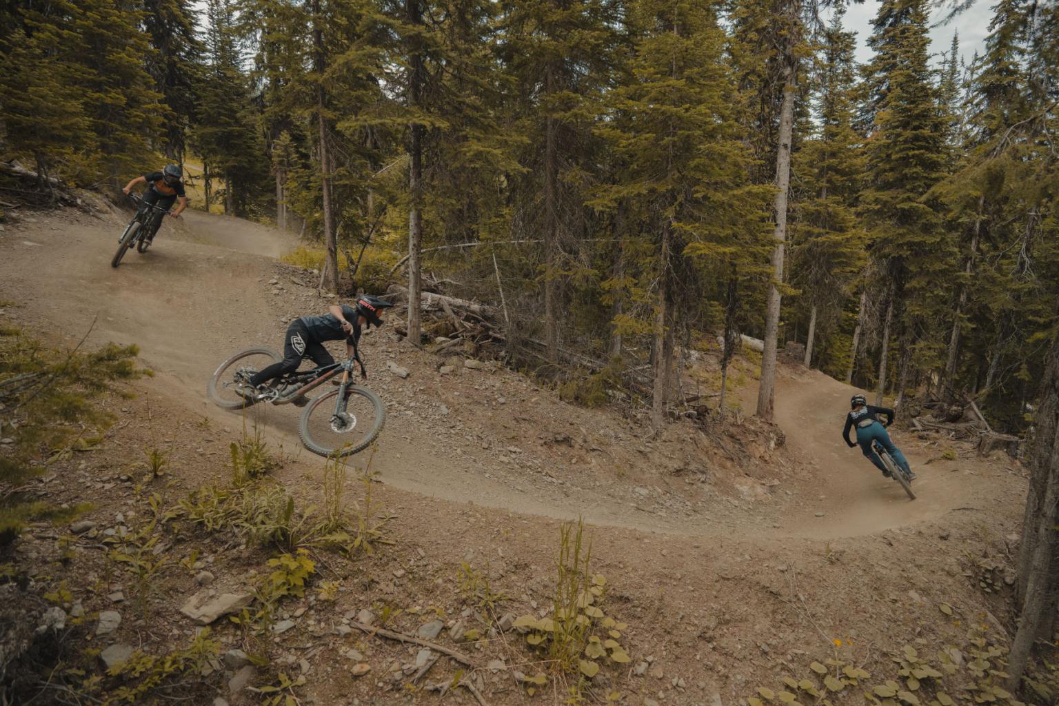 Three bikers riding on a trail surrounded by trees 