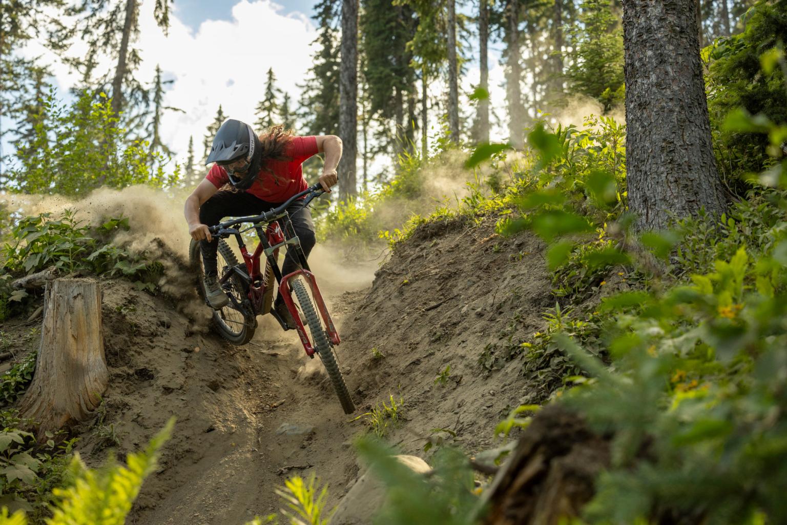 Downhill biker riding down a trail with trees in the background