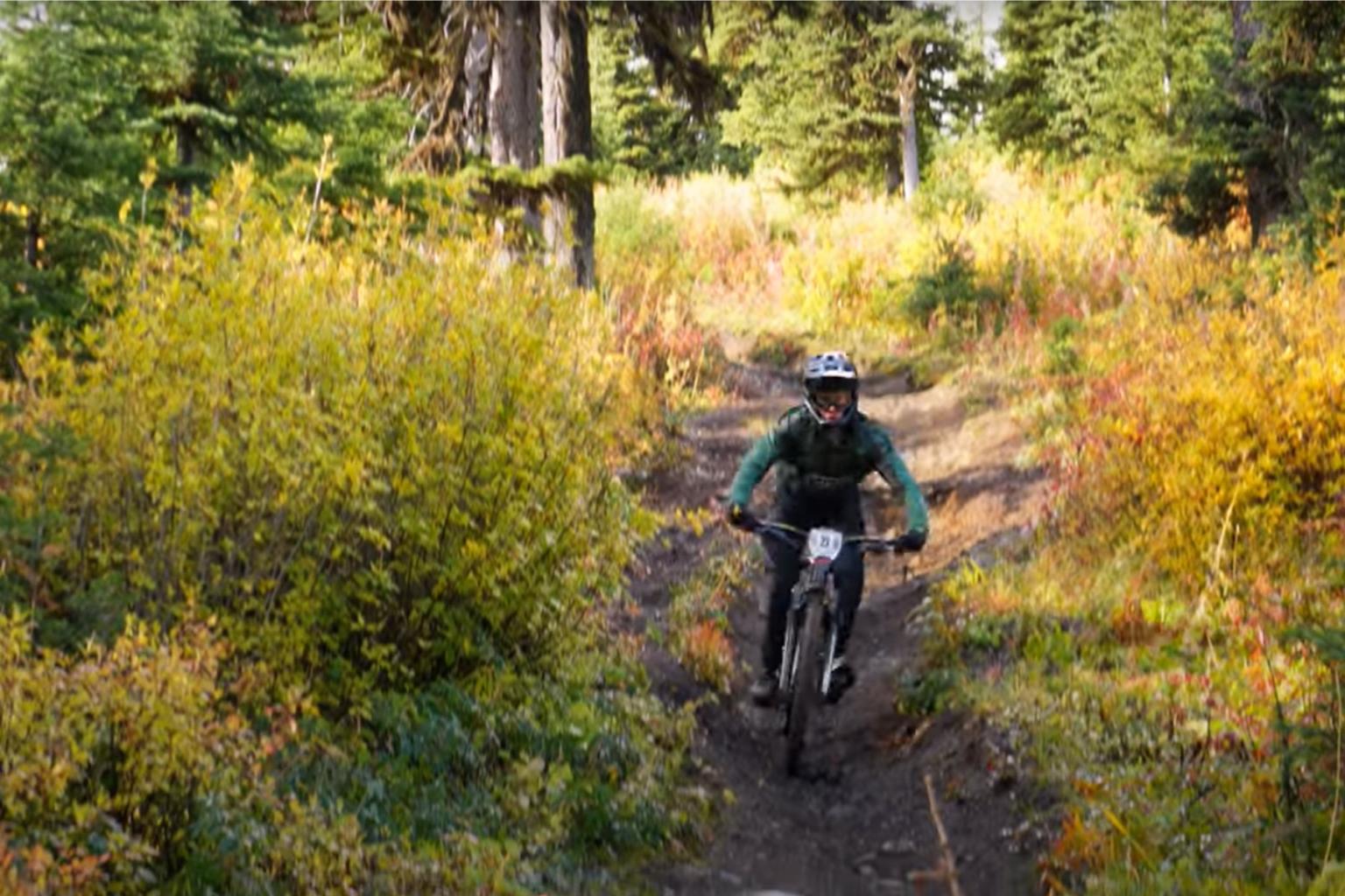 Downhill biker riding through a trail of trees 