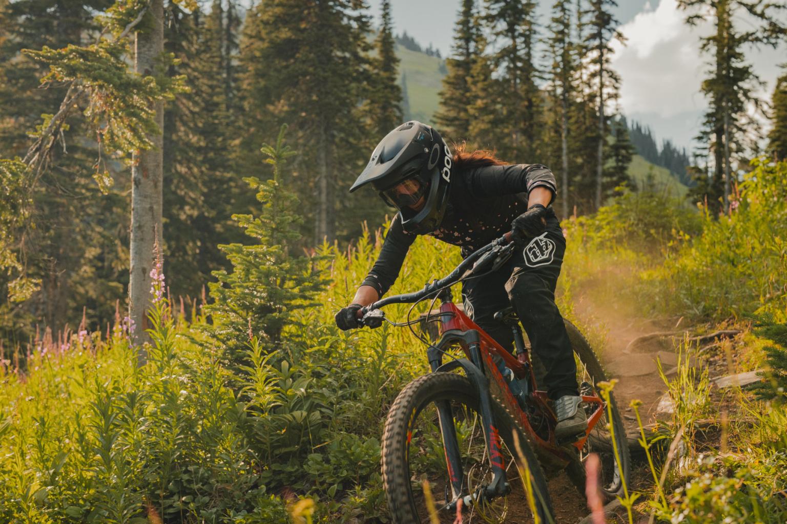 Downhill biker riding down a trail with trees in the background