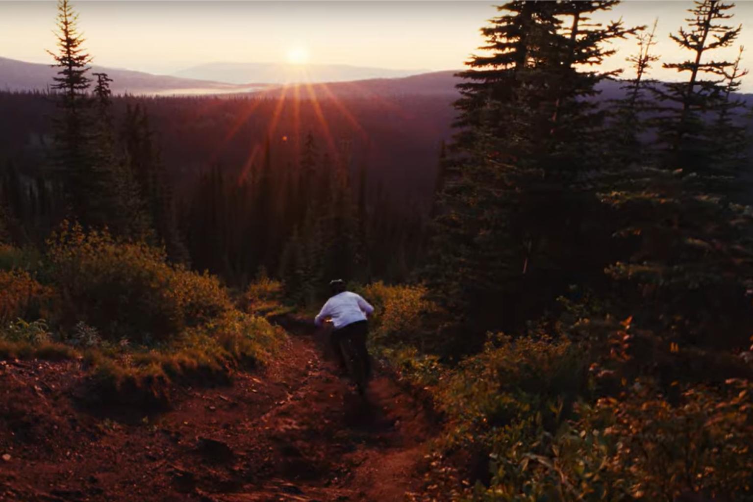 Downhill biker riding down a trail with trees in the background at sunset