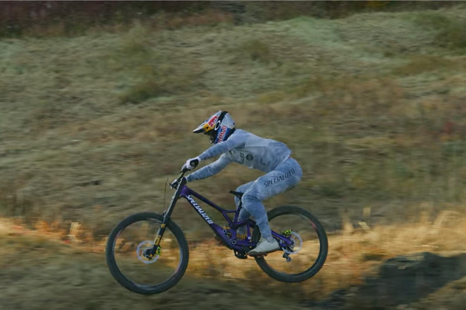 Downhill biker riding down a trail with trees in the background