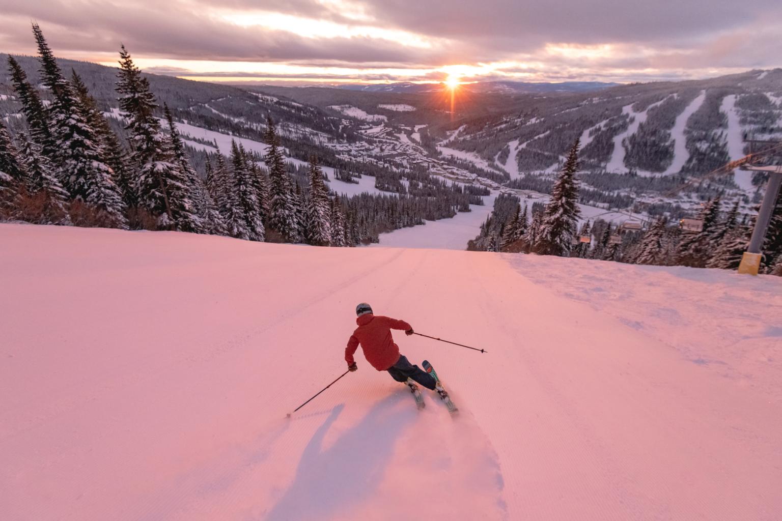 A skier riding down a freshly groomed run with mountain views in the distance