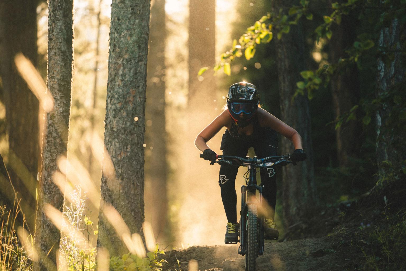 A girl downhill biking with sunlight beaming through the trees behind her