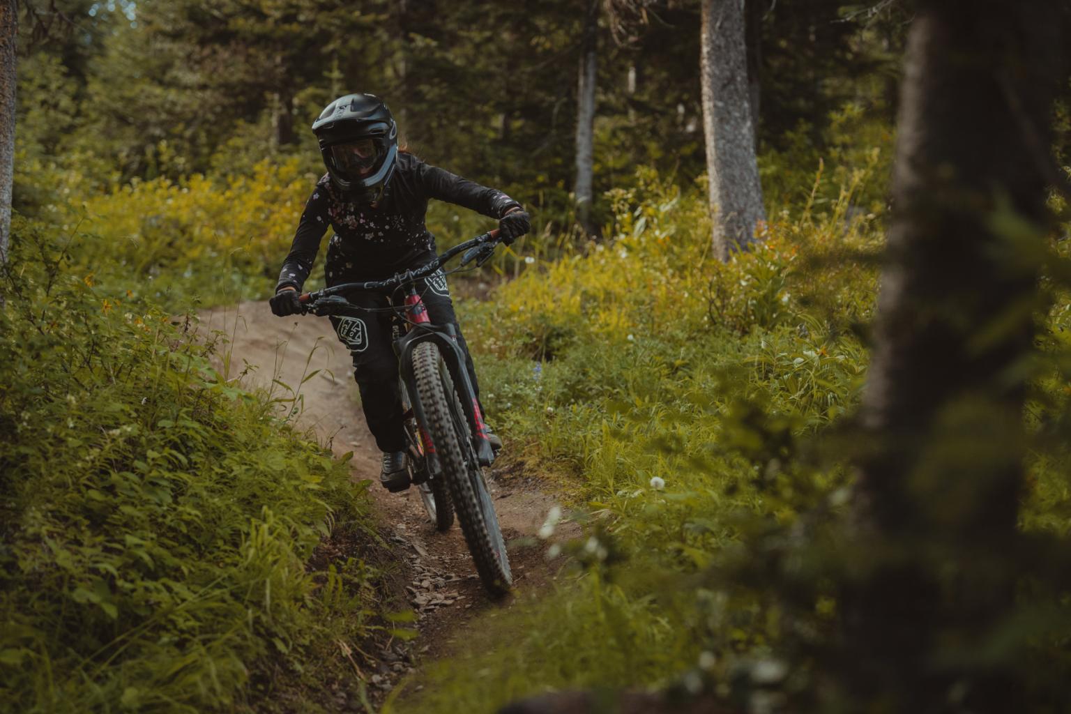 Downhill biker riding down a trail with trees in the background