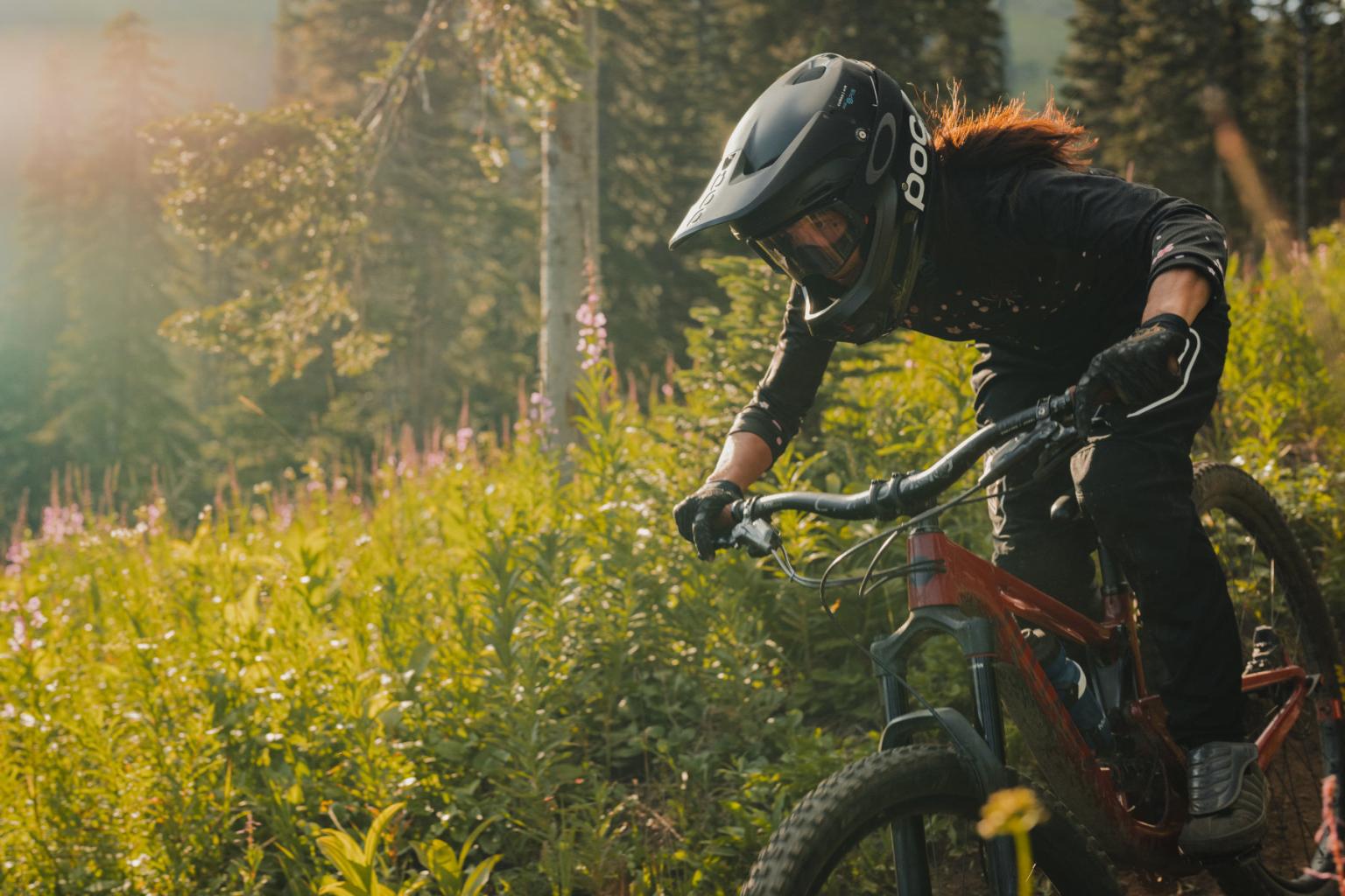 Downhill biker riding down a trail with trees in the background
