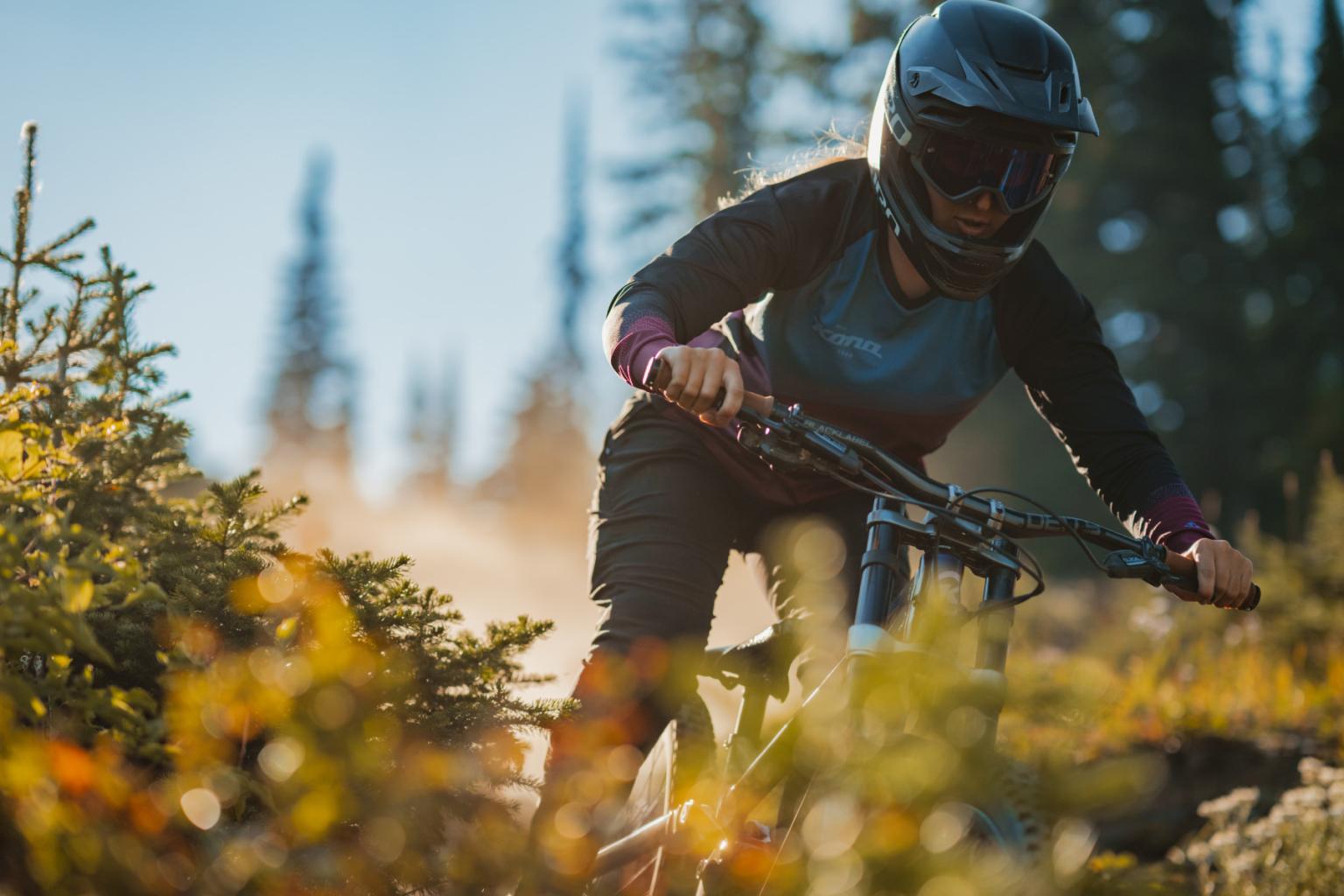 Downhill biker riding down a trail with trees in the background