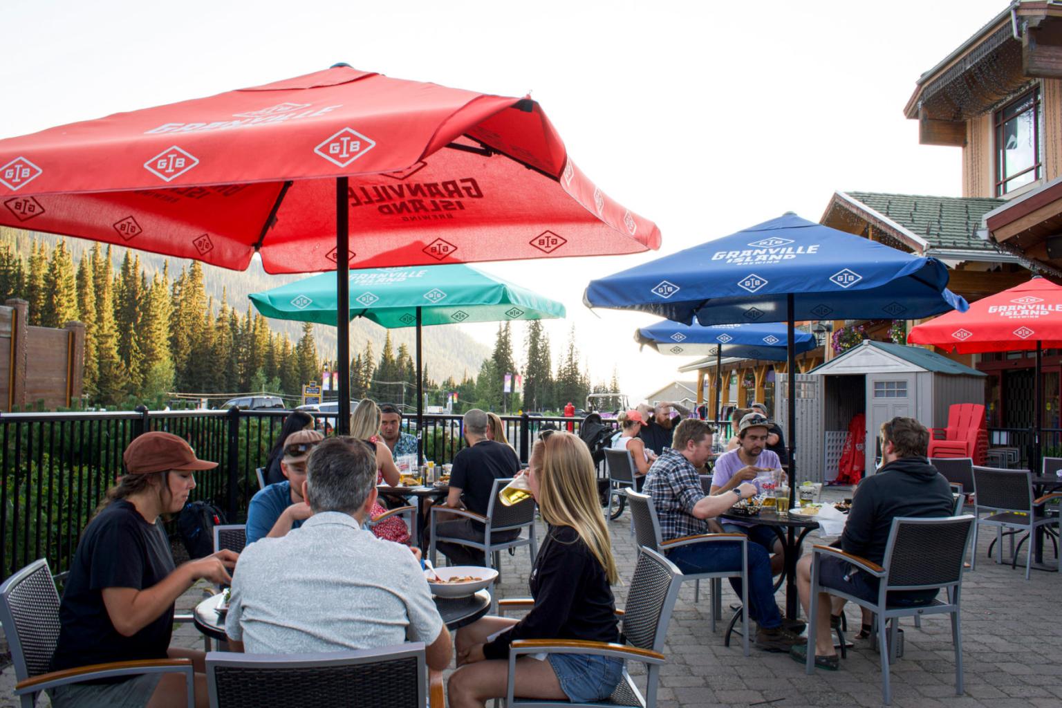 People sitting and eating on a patio in the sun with trees behind them