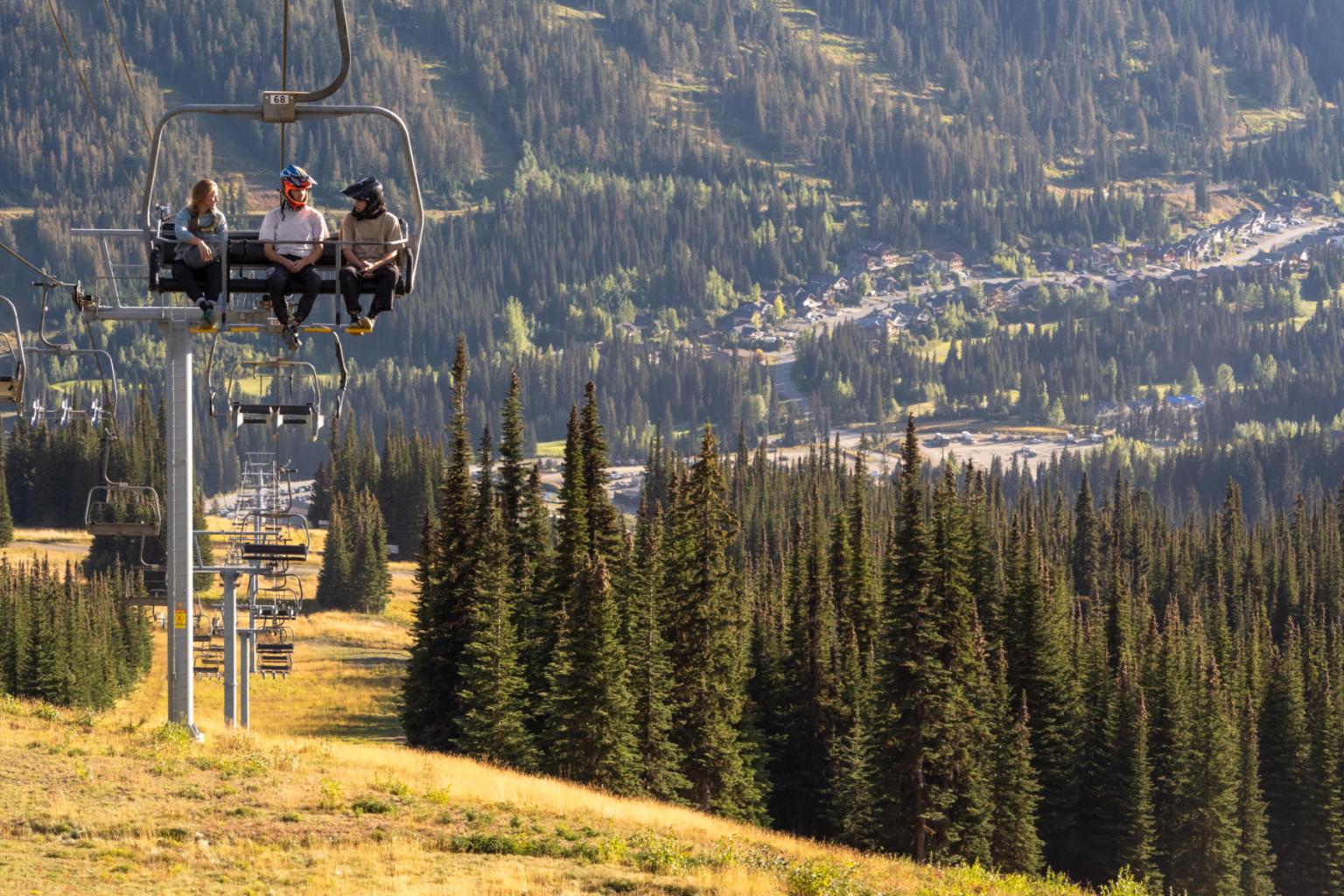 Three bikers sitting on a chairlift in the summer with the mountain in the background