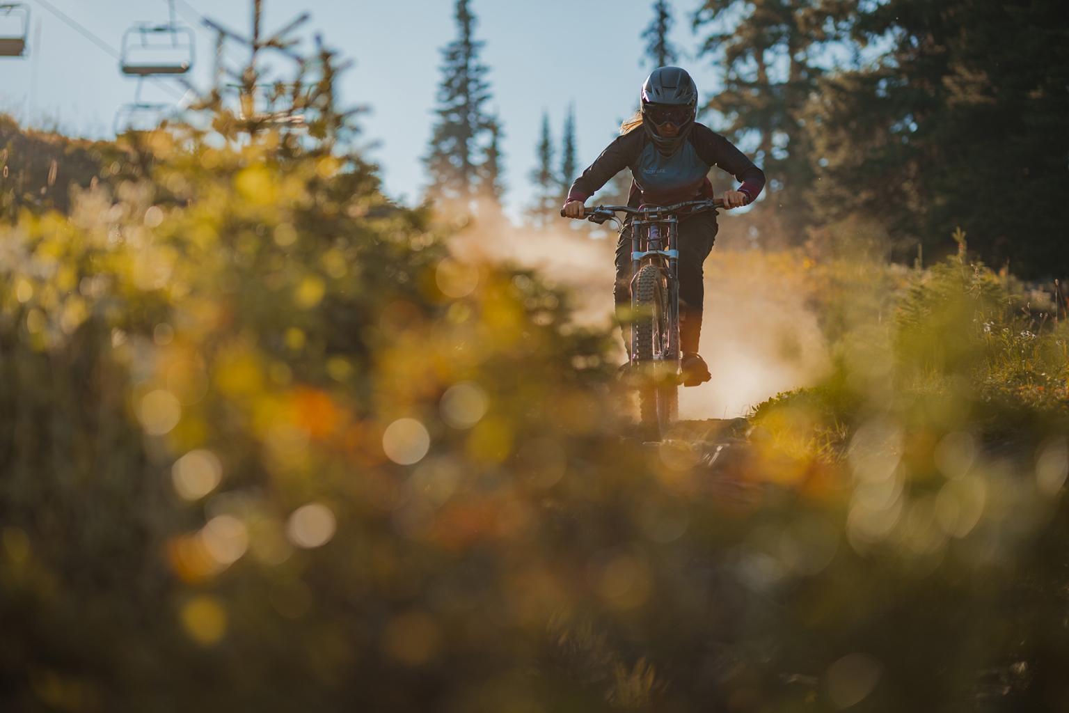 Mountain biker Kyleigh Stewart riding a tech trail at twilight with chairlift in the background.