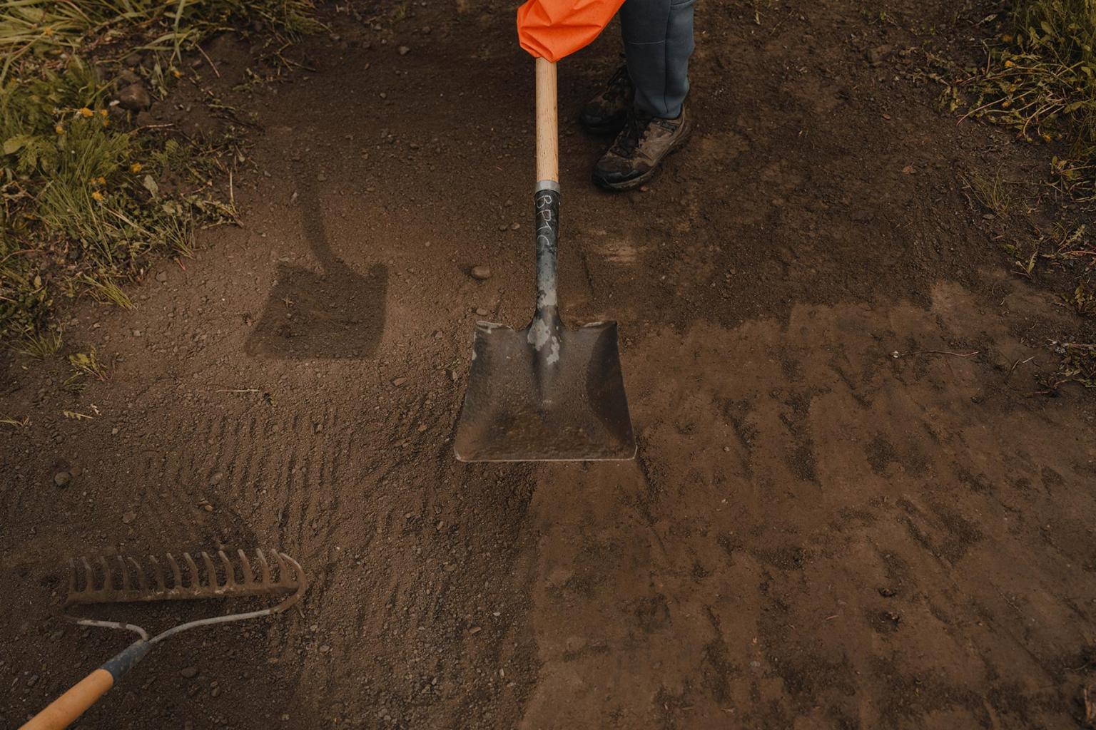 A shovel tamps down dirt on a mountain bike trail.