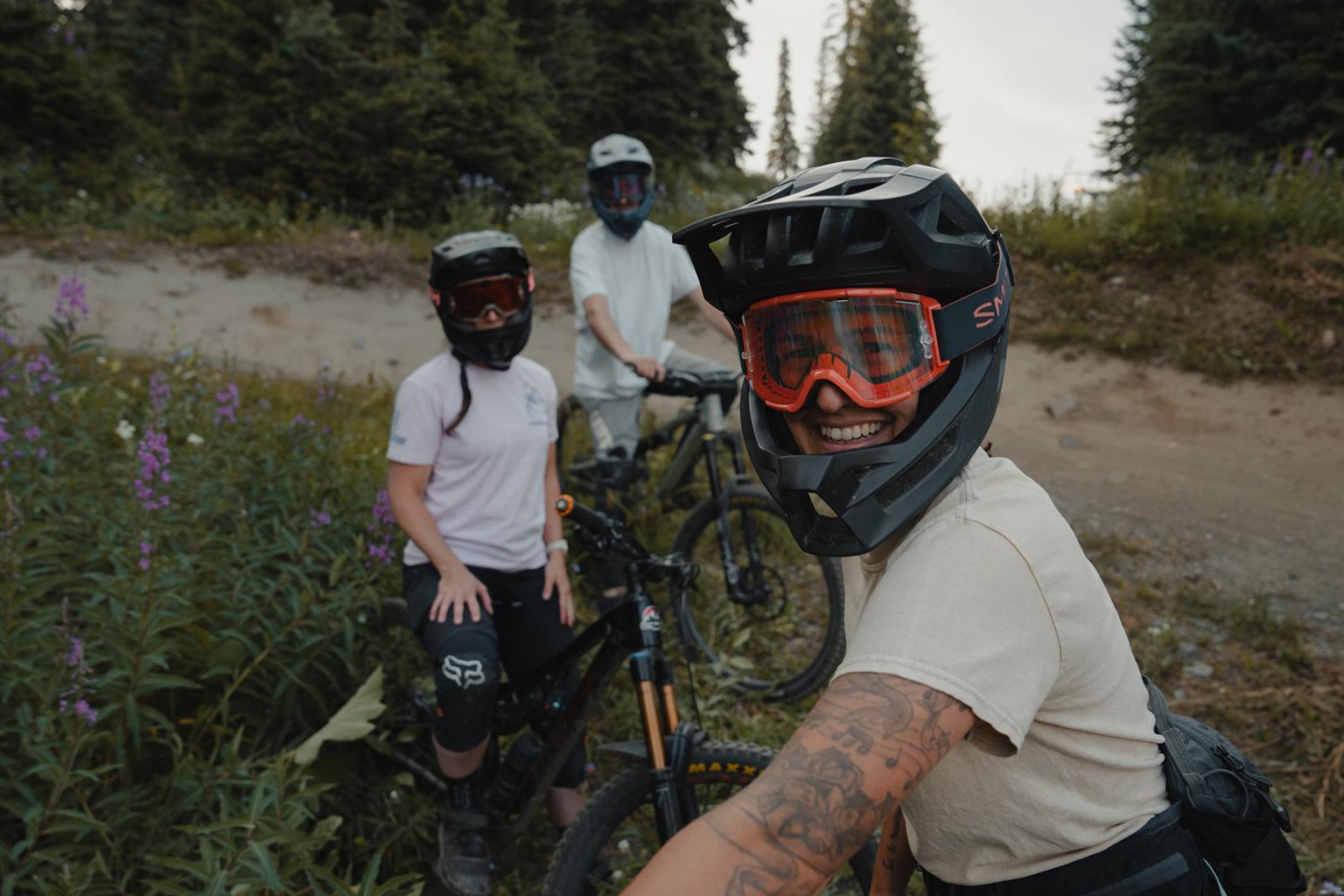 Three mountain bikers in full face helmets smile at the camera. 