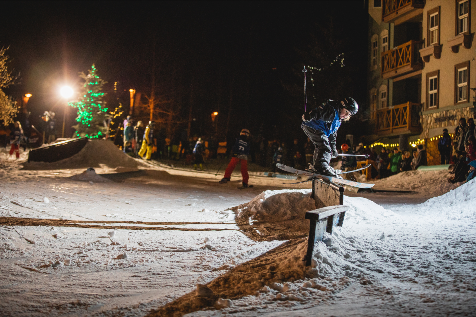 Village rail jam skiier on rail at night with lights through village stroll