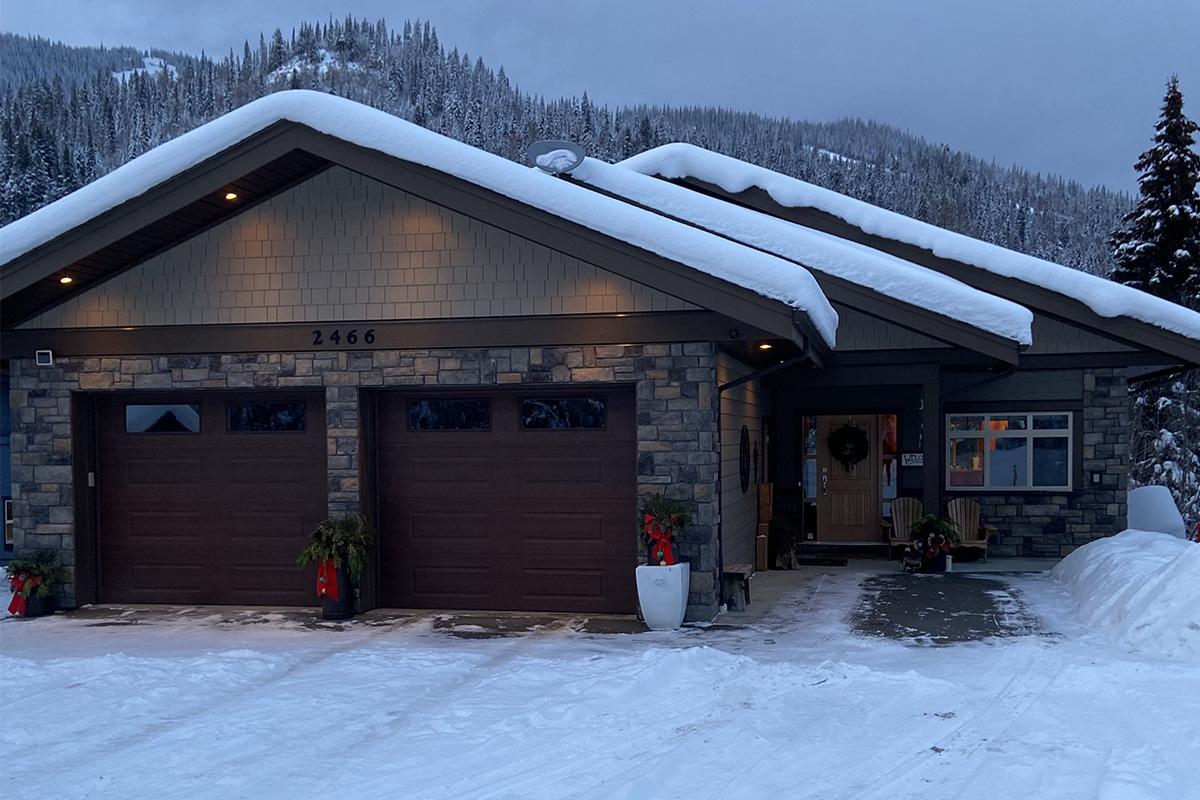 Brown brick ski chalet with snowcapped roof in front of a snowy mountain.