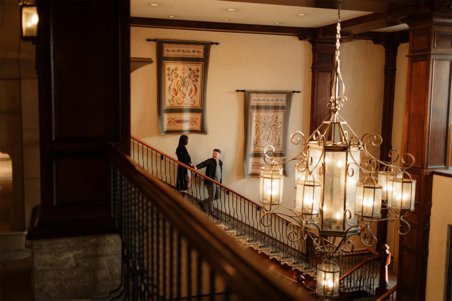 A couple talks on the stairs in the warmly lit Sun Peaks Grand hotel.