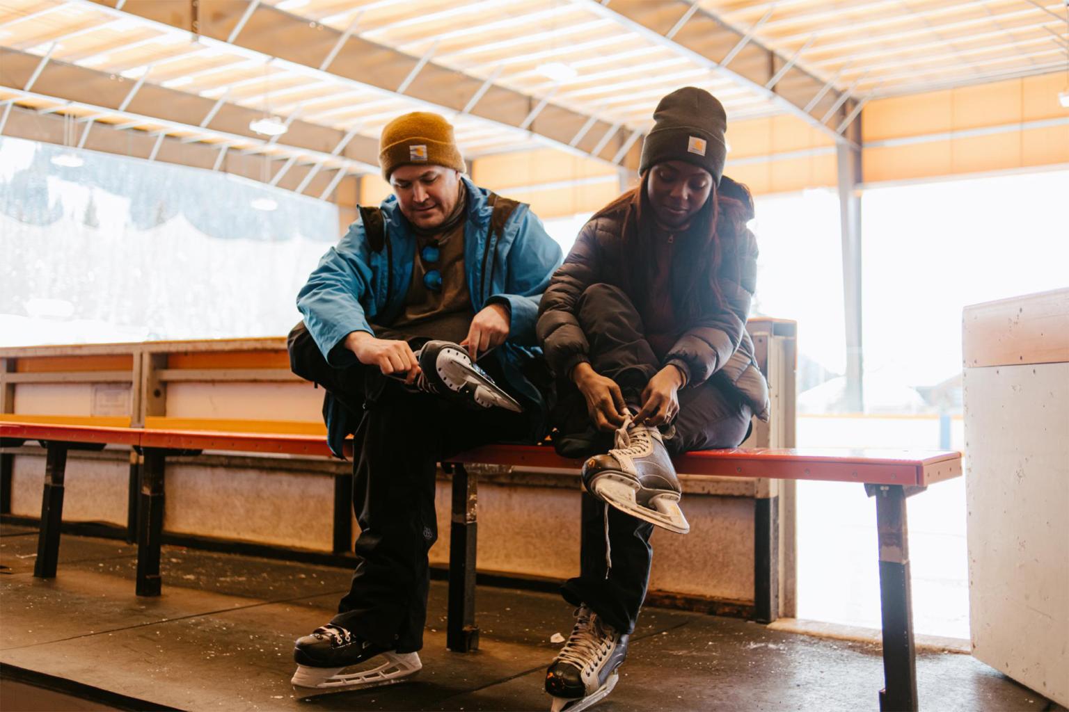 Matt and Chioma lace up their skates for an iceskating date while sitting on a bench.