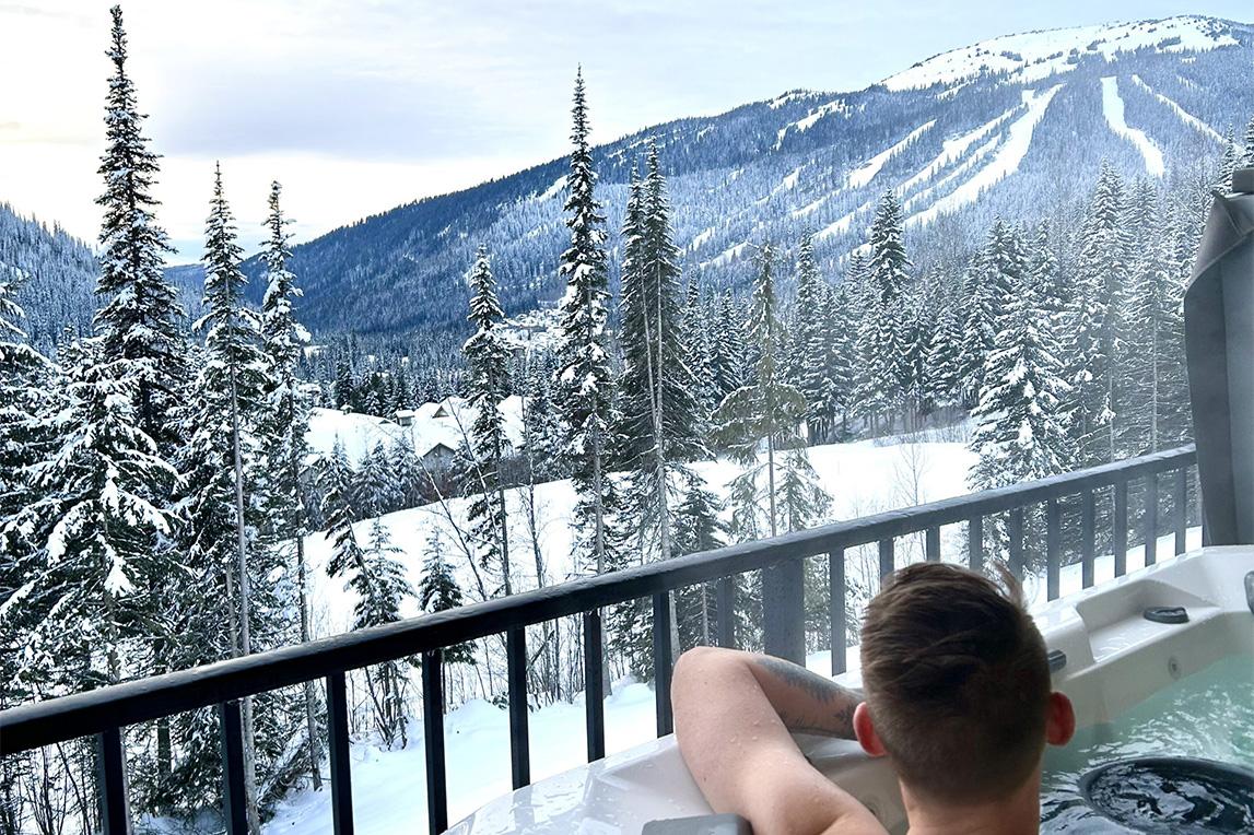 Man in a hot tub looks out over snowy Sun Peaks.