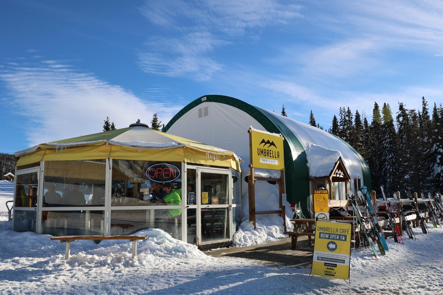 A yellow umbrella stretches over an enclosed café in winter with a red OPEN sign.