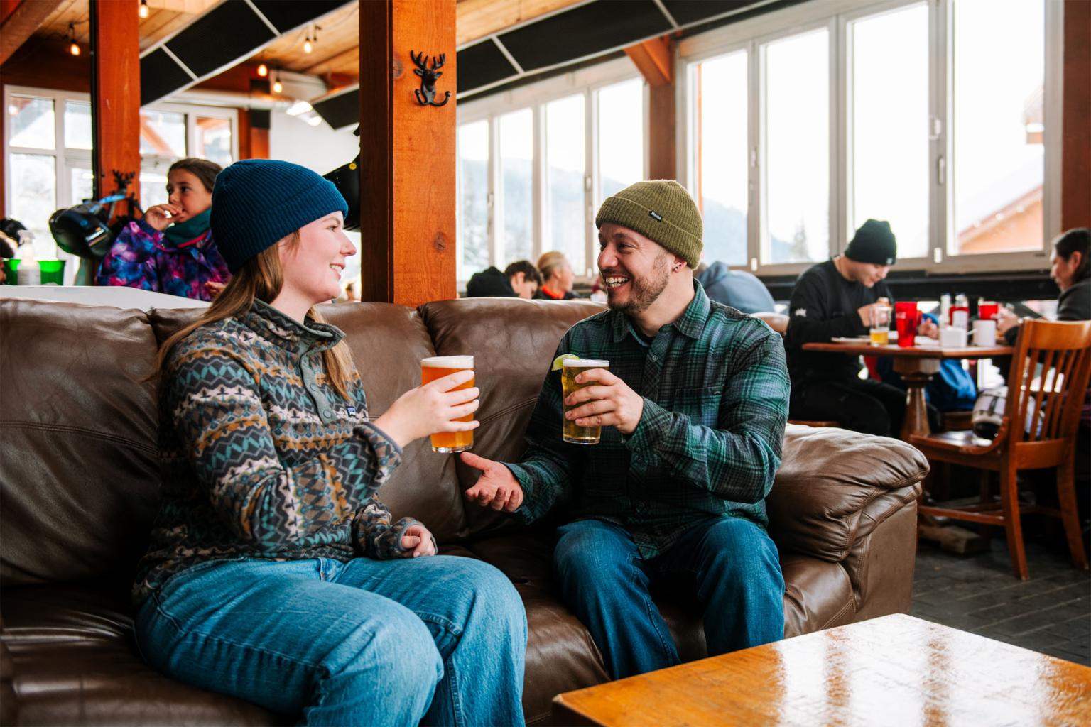 Couple smiling and toasting with beers on a couch in Bottoms Bar & Grill.