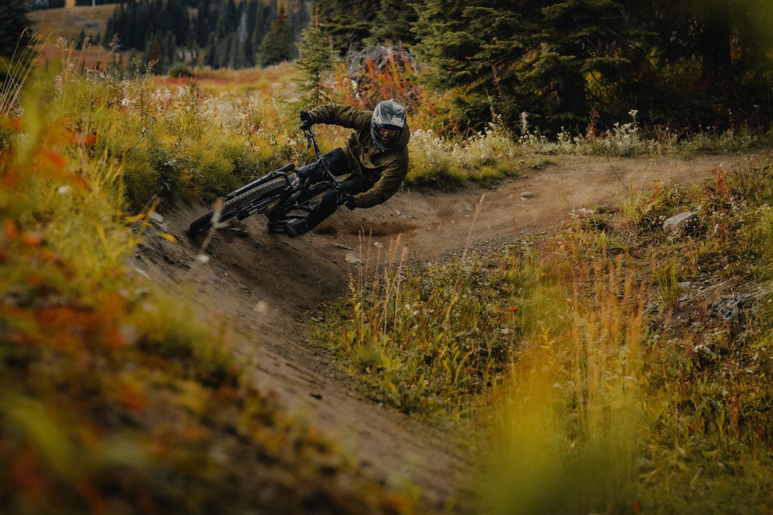 Biker racing down a dirt trail through a forest, surrounded by autumn foliage.