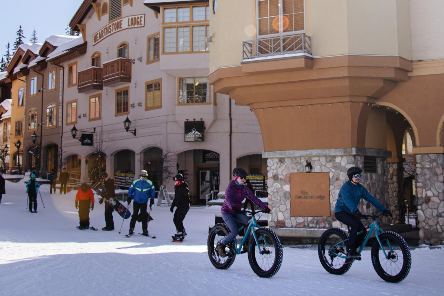 People riding fat-tire bikes through a sunny Sun Peaks village core.