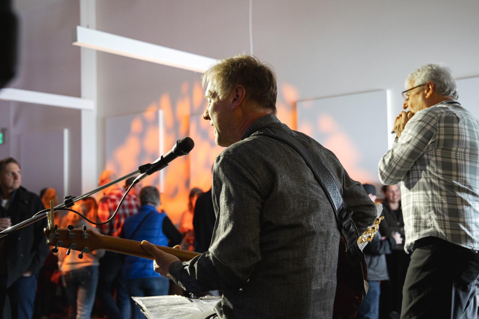Musicians performing on stage with audience in the background.