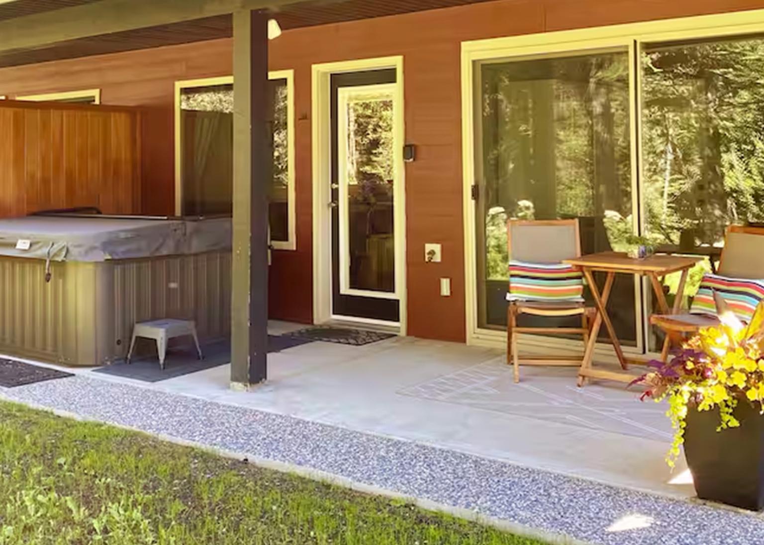 Patio with hot tub, chairs, table, and potted flowers.
