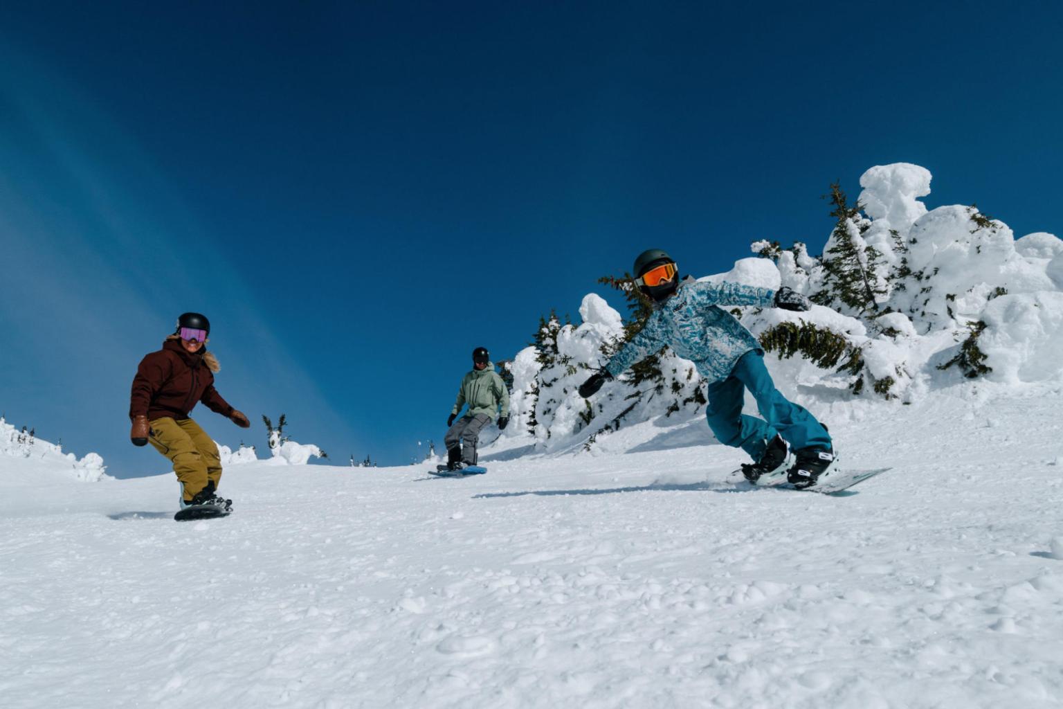 Snowboarders gliding down a snowy slope under a clear blue sky.