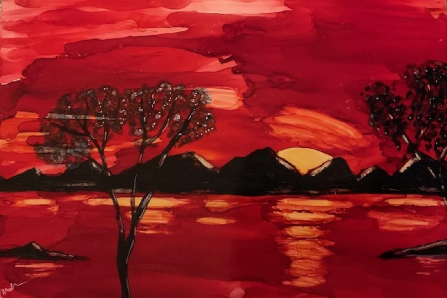 Red sunset over mountains and trees, with reflections on water.