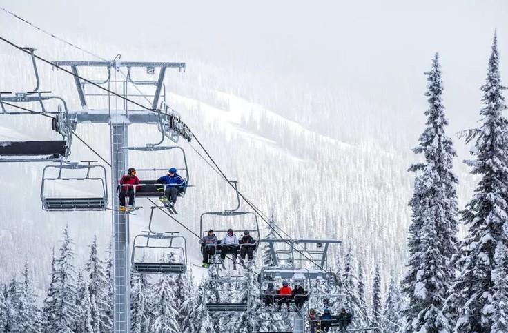 Ski lift with people ascending snowy mountain, pine trees around.