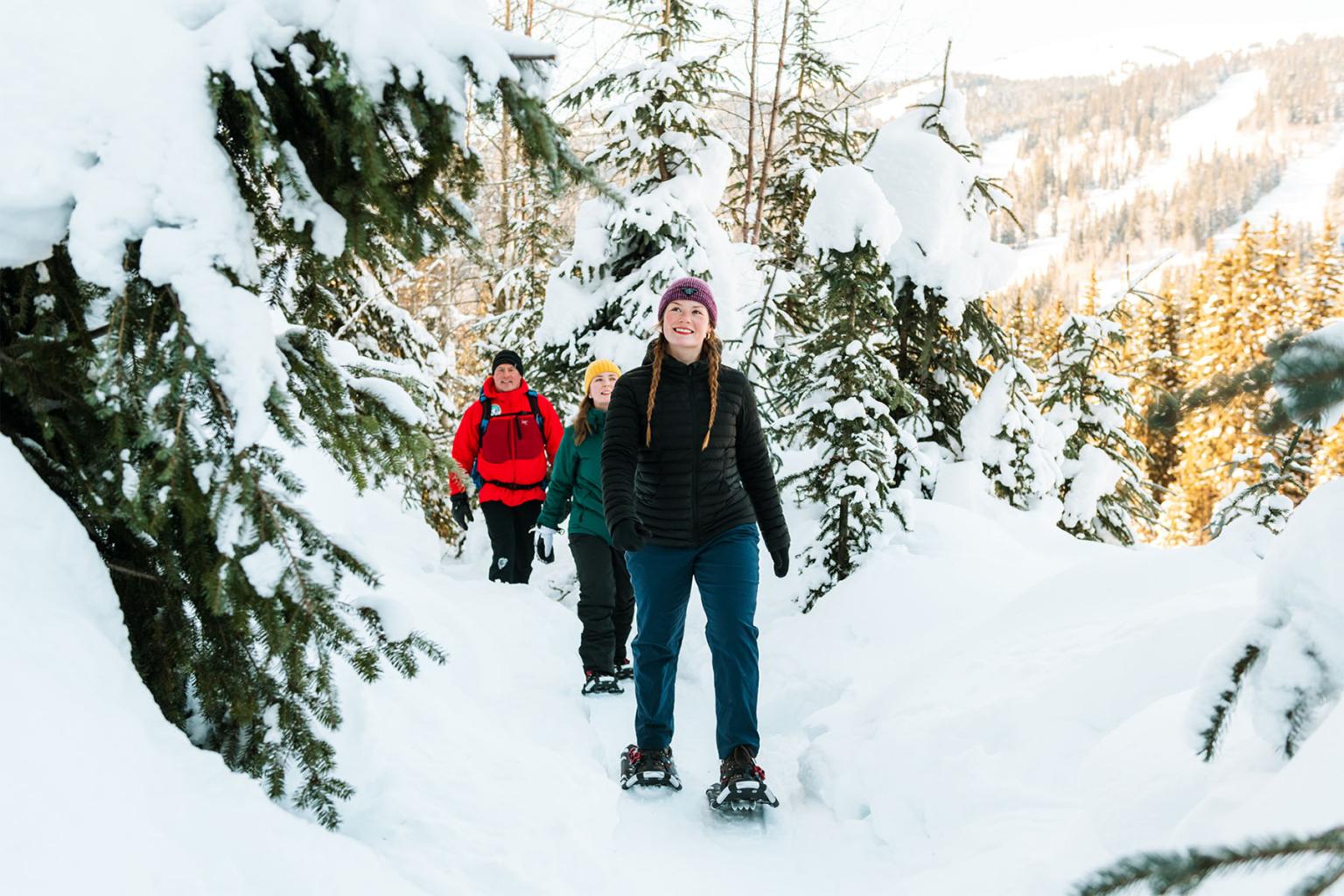 Group snowshoeing through snowy forest path.