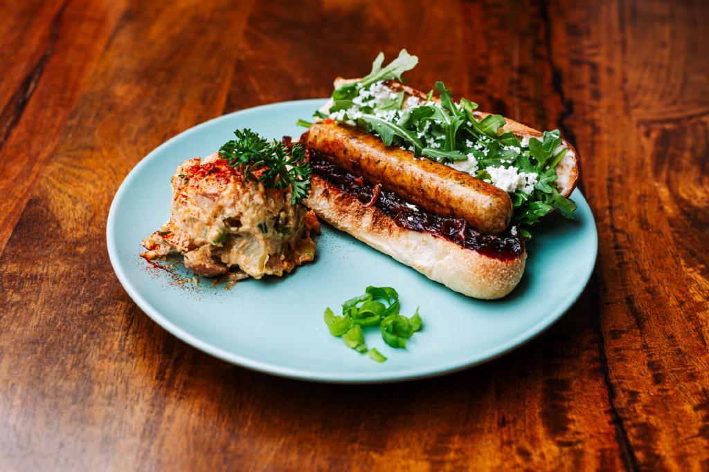 Vegan Bratwurst with greens on a plate, served with potato salad and sliced scallions.
