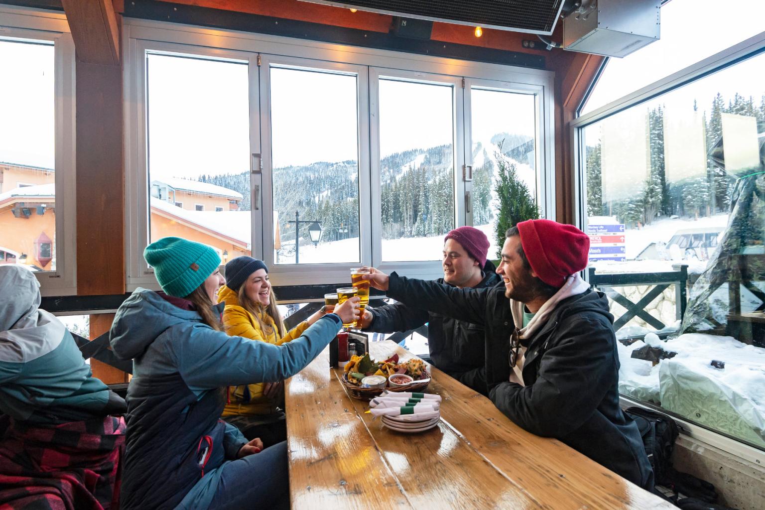 Friends toasting drinks in a cozy, snowy cabin setting.