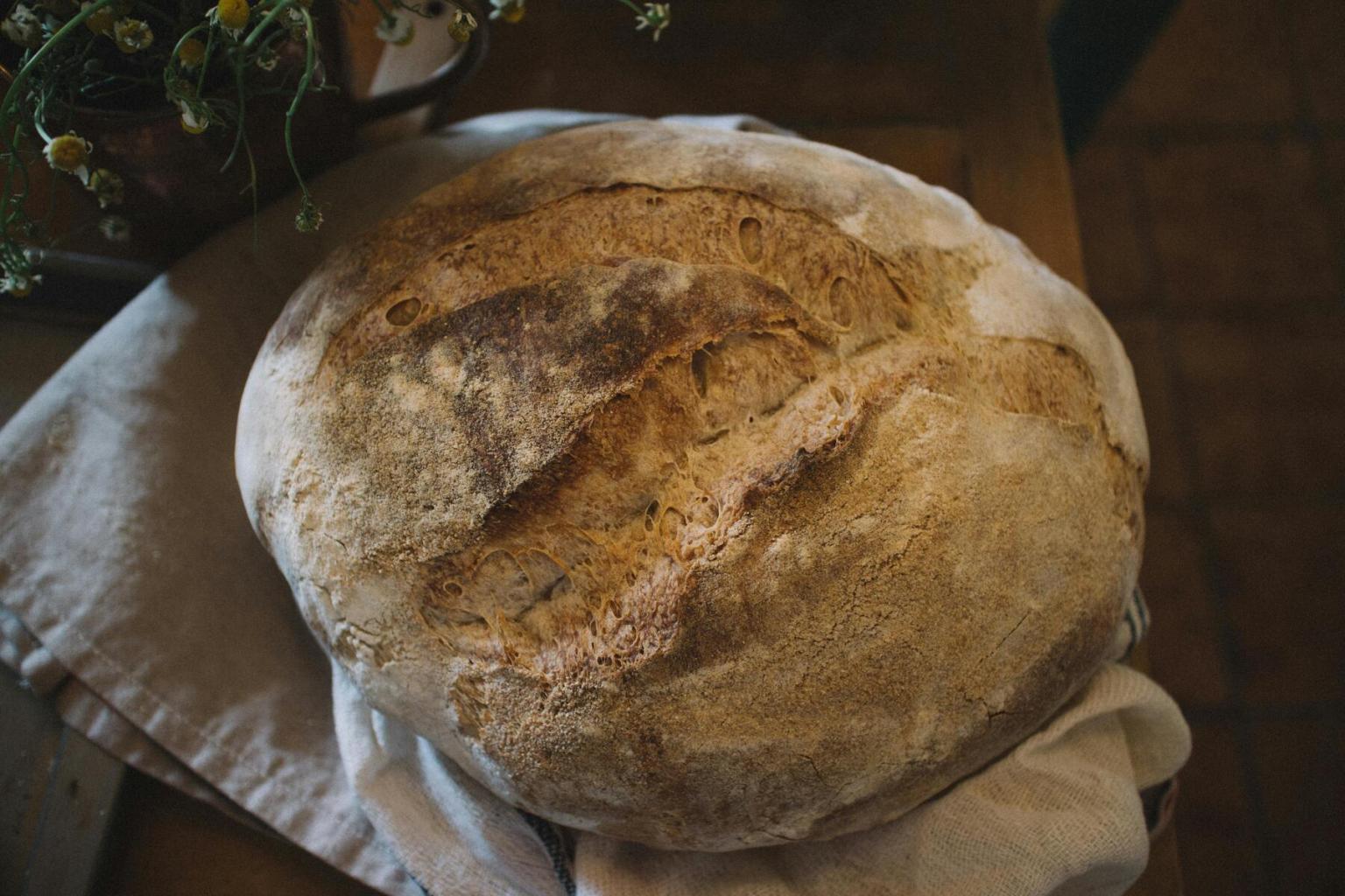Crusty round loaf of bread on a cloth, dimly lit setting.