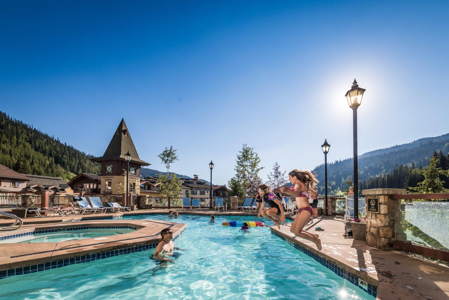 Mountain resort pool with children playing under a clear blue sky.