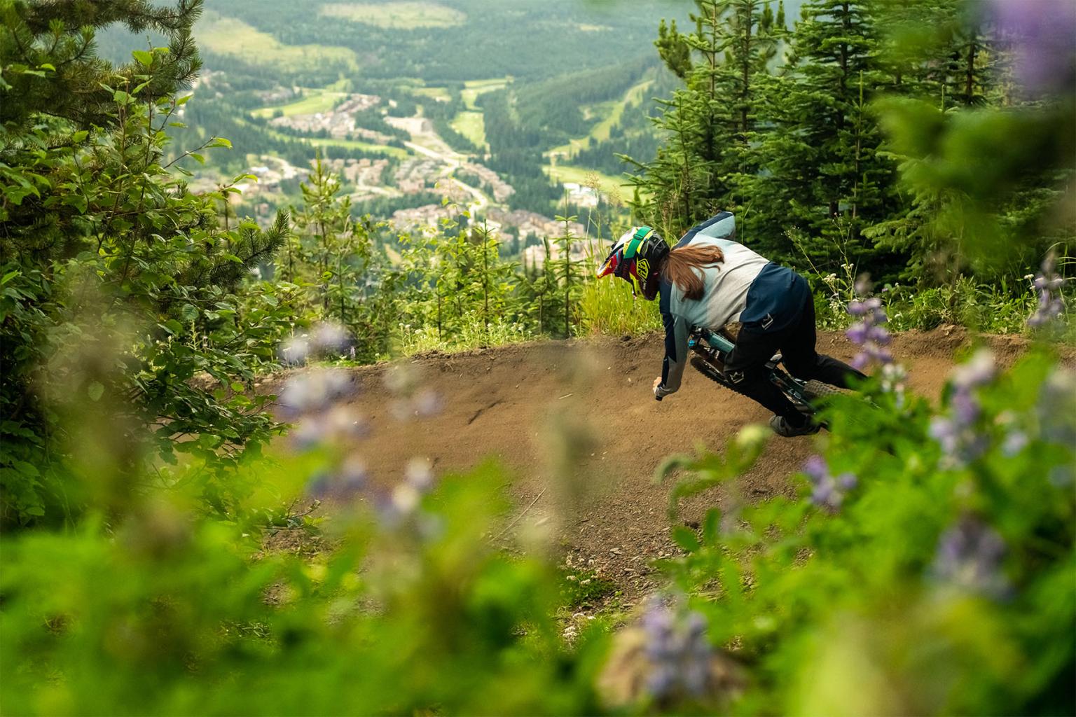 Mountain biker racing down a forest trail with a scenic valley view.