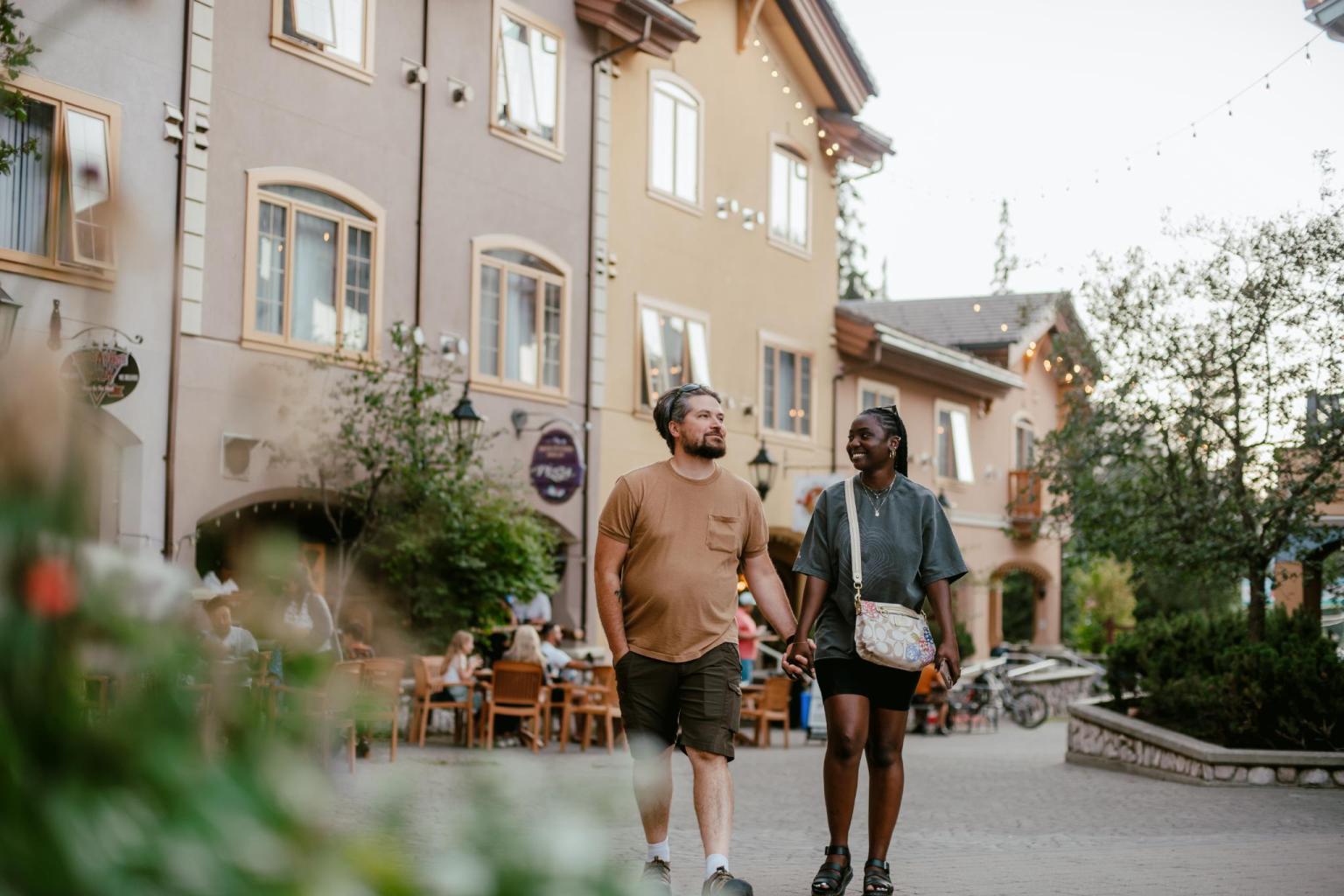 Couple holding hands, walking in a quaint village setting.